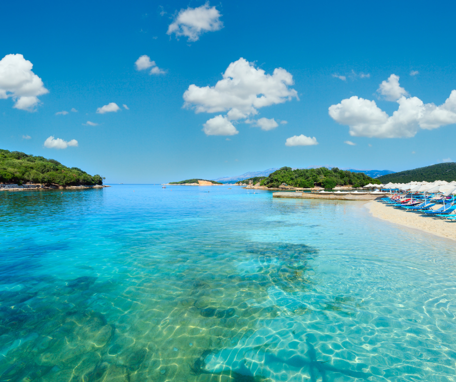 a view of the beach and mountains from a boat (1) a sandy beach with blue water and umbrellas